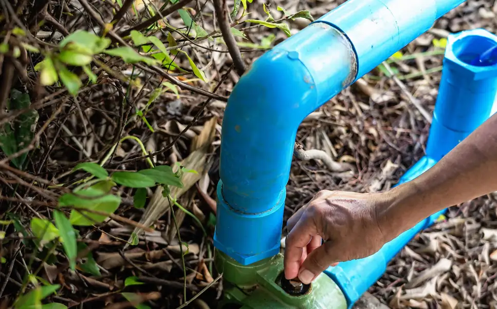 A hand turning a valve on a blue PVC water pipe outdoors